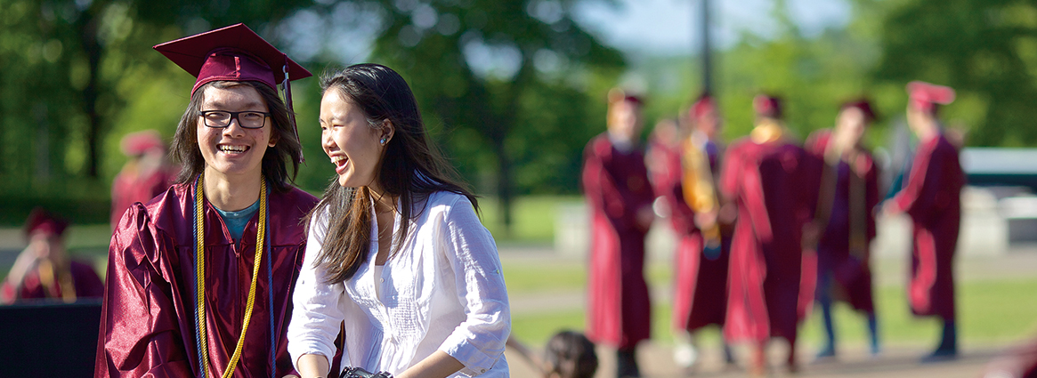 Graduate student laughing with a family member while other graduates gather in the background