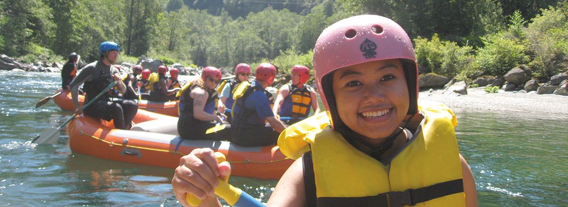 Whitewater Rafting student smiling while rafting with fellow rafters behind her