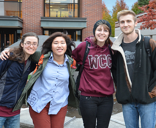 Four students smiling in front of Orca Central located in the Heiner Building