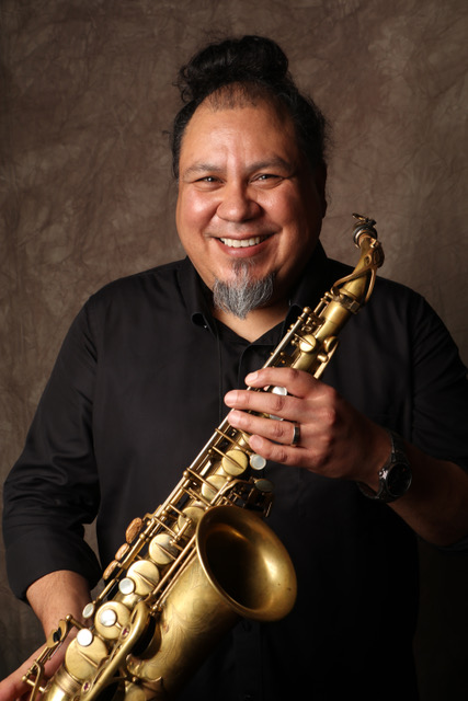 Faculty member Michael Paul Gurule against a brown background holding a saxophone