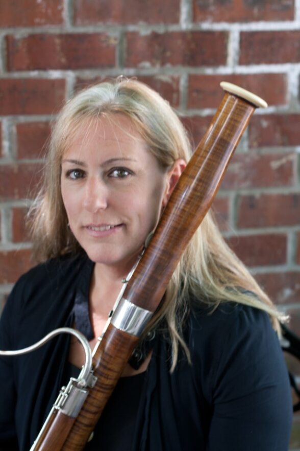 Faculty member Pat Nelson against a brick background holding a bassoon