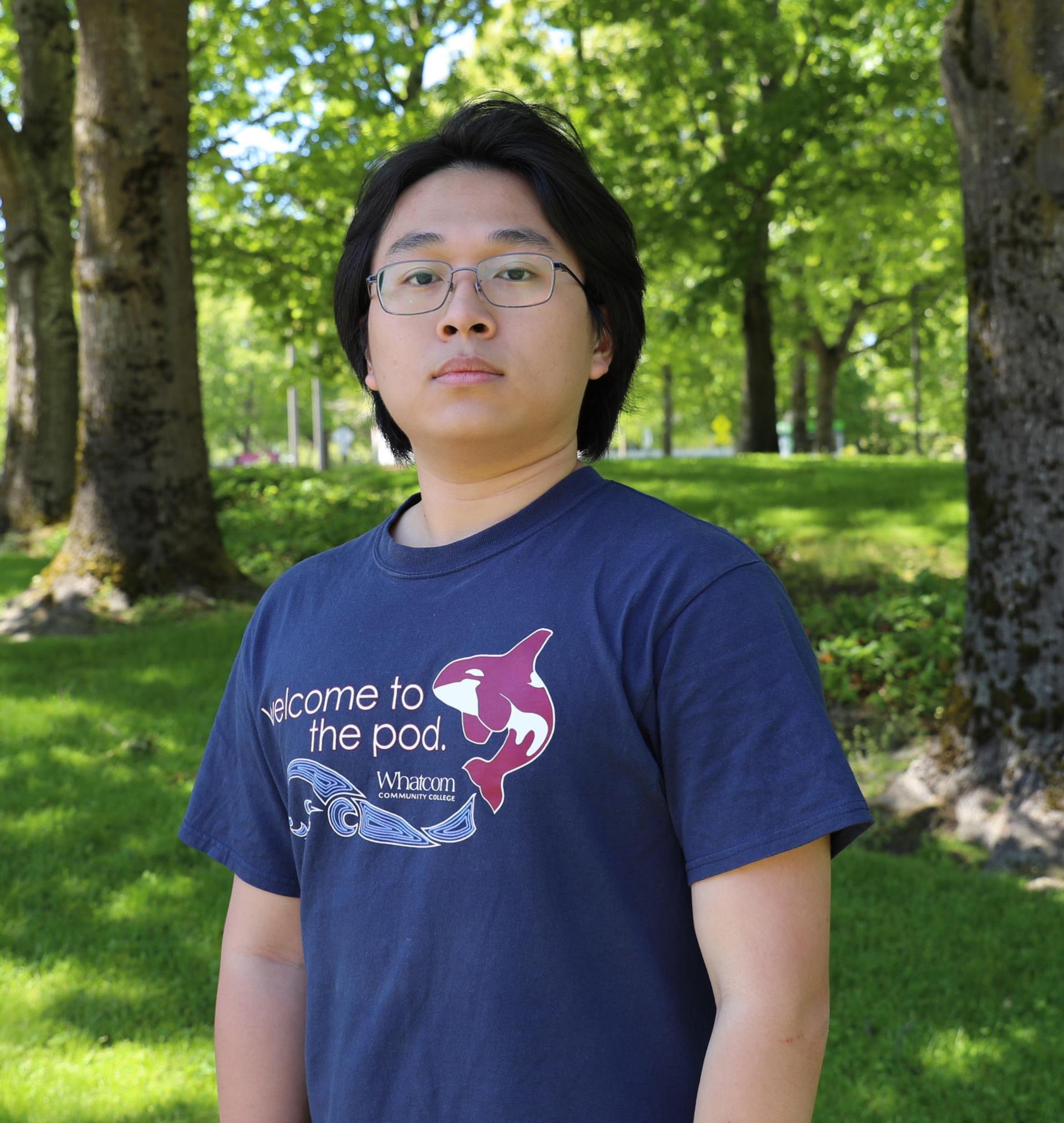 Photo of Pod Leader Bao Truong standing in front of a grassy tree area with a shirt that reads Welcome to the Pod